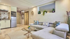 Una sala de estar moderna con sofá, mesa de centro y una cocina con refrigerador y microondas.