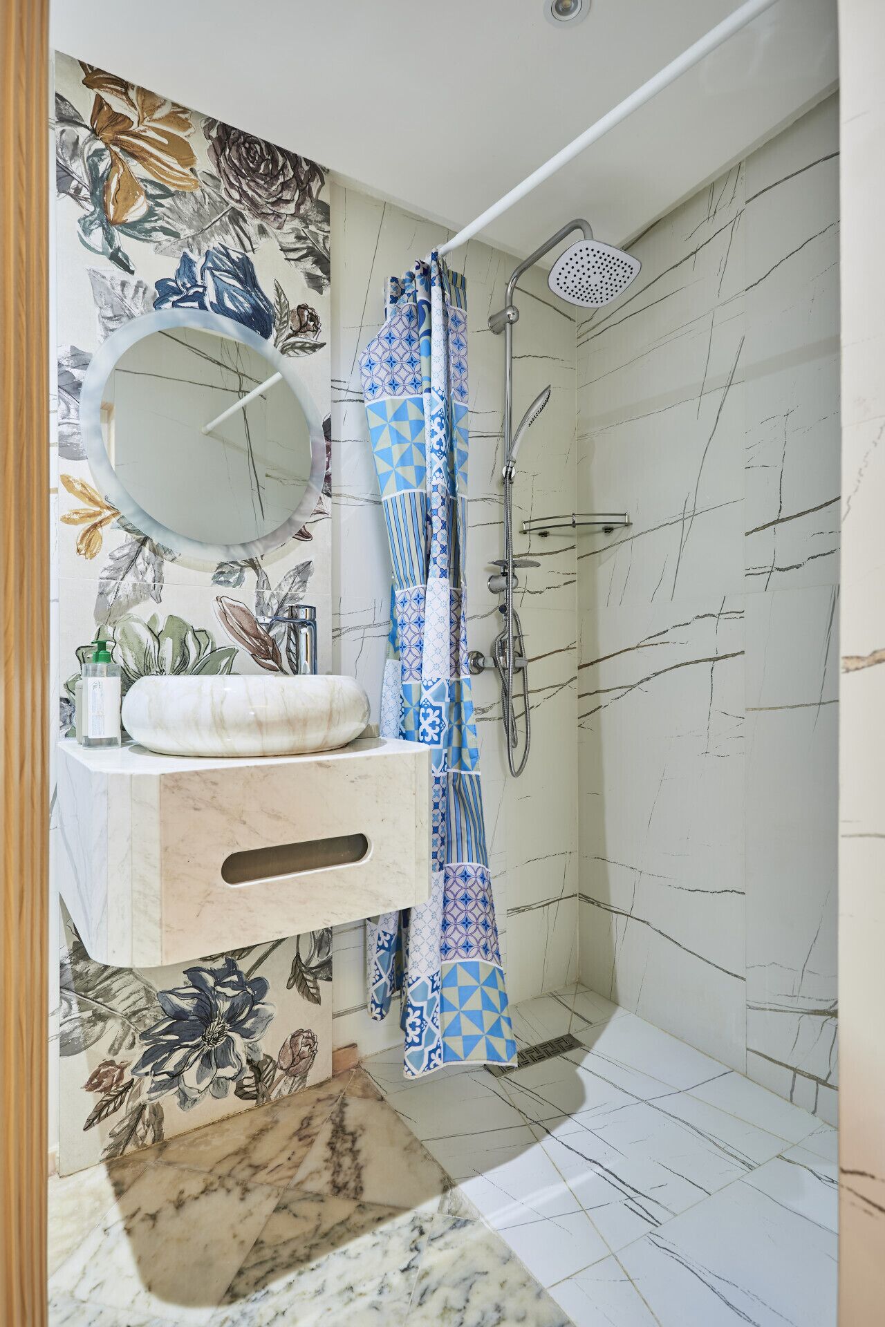 A bathroom with a marble sink, a mirror, a shower with a handheld showerhead, and a patterned shower curtain.