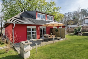 A red house with a tiled roof, a patio with a table and chairs, and a garden. - Modern semi-detached house on the lake with terrace & lake view (Korswandt)