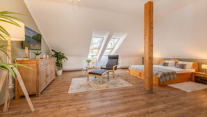 Un dormitorio con techo inclinado, muebles de madera, una cama con manta escocesa, una silla, una mesita con una planta y un cuadro en la pared.