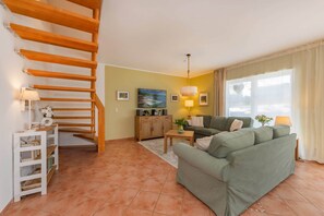 A living room with a wooden staircase, a green sofa, a wooden cabinet, and a painting on the wall. - Modern semi-detached house on the lake with terrace & lake view (Korswandt)