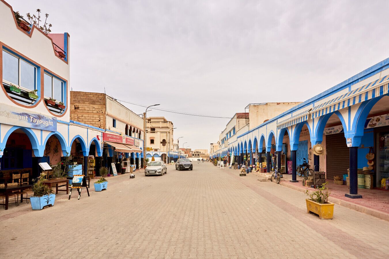 A street lined with shops and restaurants, featuring blue arches and a paved road.