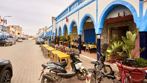 Een straat met terrasjes, een gebouw met blauwe bogen en geparkeerde voertuigen.