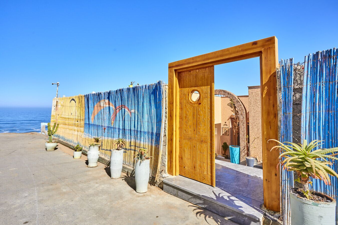 A coastal building with a wooden door, a mural, and potted plants.