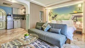 Een moderne woonkamer met een bank, een glazen salontafel en een keuken op de achtergrond.