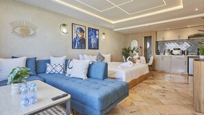 A modern hotel room with a sofa, a bed, a dining area, and a kitchen.