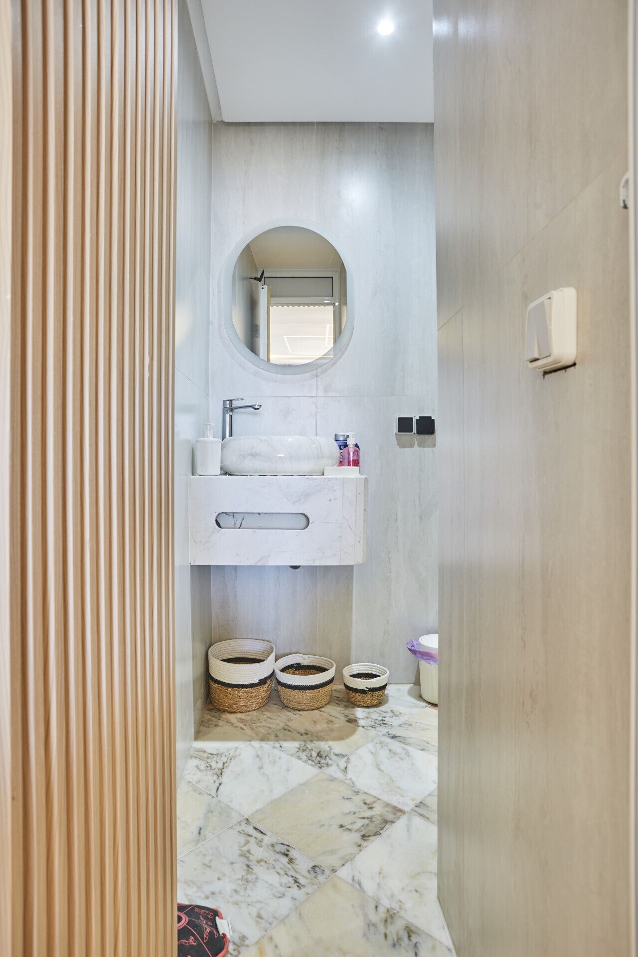 A modern bathroom with a marble floor, a round mirror, a white sink, and a toilet.