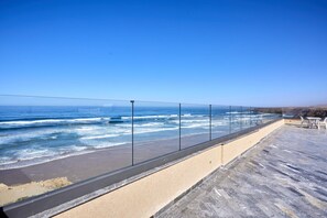A seaside terrace with a clear view of the ocean, a sandy walkway, and a seating area with tables and chairs.