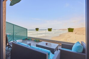 Une vue sur la plage depuis un balcon agrémenté de meubles en osier, d’un paravent en treillis vert et de jardinières suspendues.