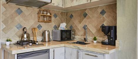 A kitchen with a dishwasher, microwave, kettle, and coffee maker on the counter.
