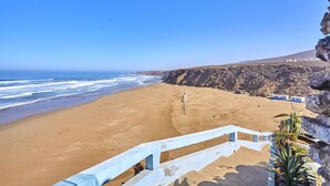 Una playa con una barandilla blanca, un acantilado rocoso y un cielo azul despejado.