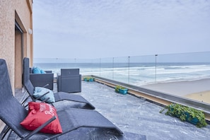 A balcony with wicker chairs and cushions, overlooking a beach with waves. - Wake to Waves: Stylish 1-Bedroom by the Shore (Mirleft)