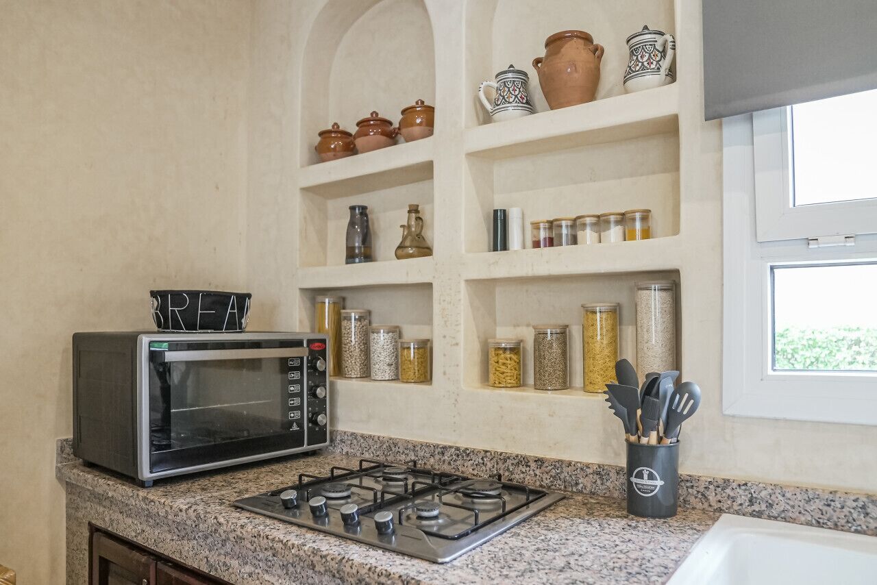 Une cuisine équipée d’un four à micro-ondes, d’une cuisinière à gaz, d’étagères remplies de bocaux et d’une fenêtre.