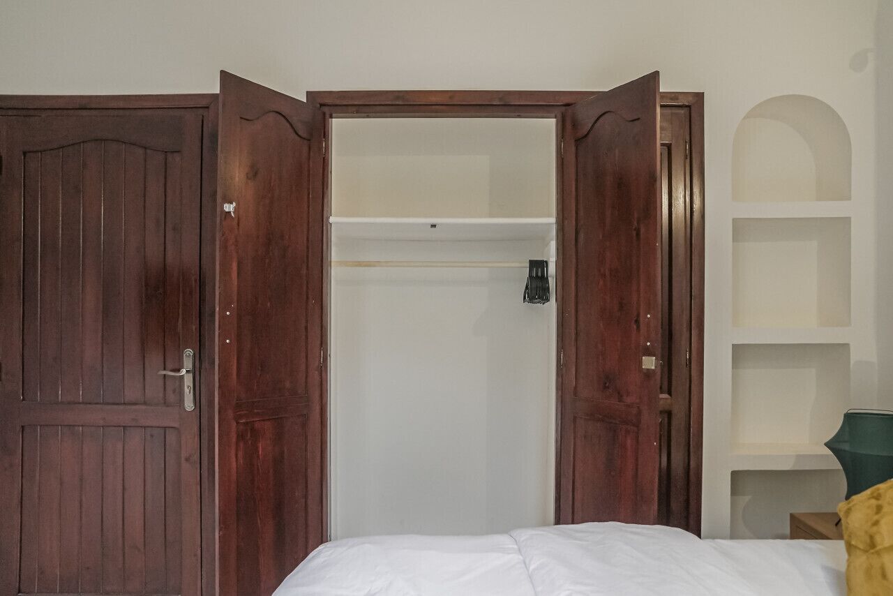 A room with a bed, a wardrobe, and a shelf unit.