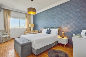 A bedroom with a large bed, a nightstand, a chair, a desk, and a view of the city through the window. - Spacious 2 Bed Flat with City Views & Free Parking (Dar-el-Beida)
