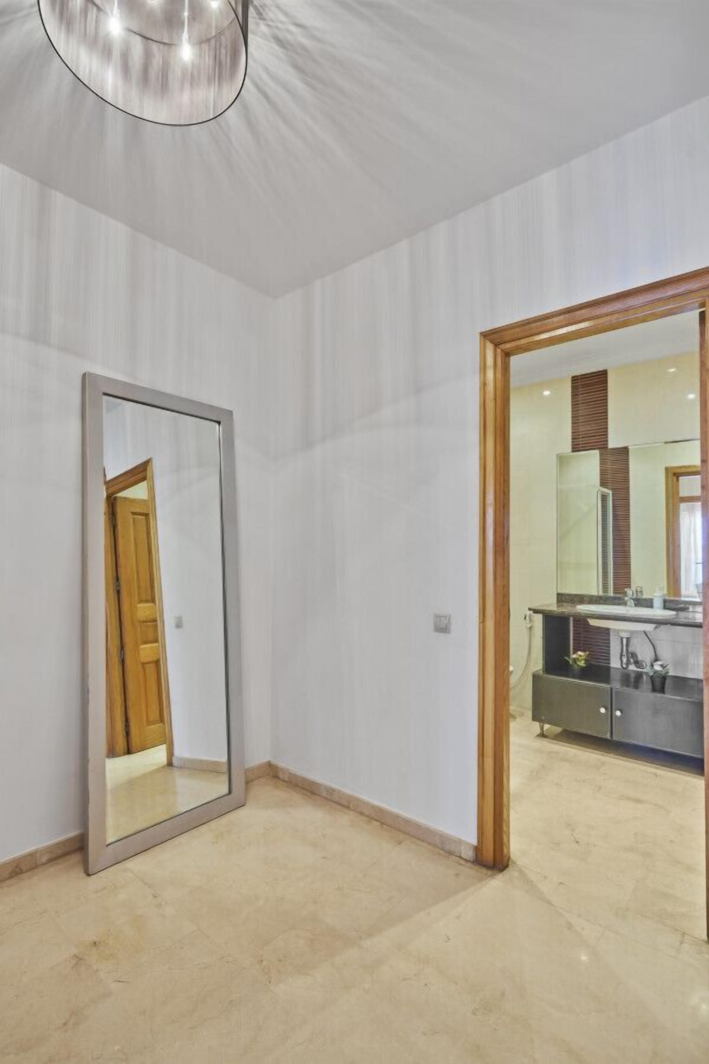 A room with a large mirror, a wooden door, and a view into a bathroom with a sink and cabinets.