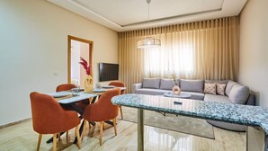 Uma sala de estar moderna com sofá, mesa de jantar e cadeiras. Há uma televisão na parede e um vaso decorativo na mesa.