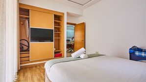 Quarto de hotel com cama, televisão, guarda-roupa e casa de banho visível através de uma porta aberta.