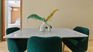 Un comedor con una mesa de mármol, sillas tapizadas en verde y un jarrón blanco con plantas amarillas y verdes.