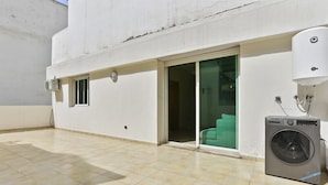 Un espacio exterior limpio y moderno con lavadora, puerta corredera de vidrio y una ventana pequeña.