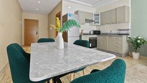 Una cocina moderna con encimera de mármol, sillas verdes y un refrigerador.