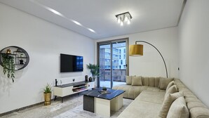 Ein modernes Wohnzimmer mit Sofa, Couchtisch, Fernseher und einem großen Fenster.