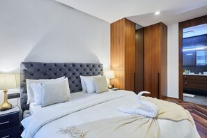 A hotel room with a tufted headboard, a bed with white linens, a wooden wardrobe, and a mirror. - Modern 2 Bed in Casa Finance City W/ Free Parking (Casablanca)