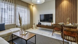 Ein modernes Wohnzimmer mit Sofa, Couchtisch, Fernseher, Wandverkleidung aus Holz und einem Essbereich mit Stühlen und Tisch.