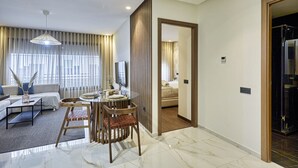 Ein modernes Hotelzimmer mit einem Glastisch, einer Couch, einem Fernseher und einem großen Fenster mit Vorhängen.