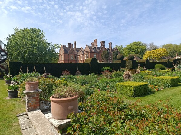 A large, historic building with a well-maintained garden featuring hedges, potted plants, and a lawn.