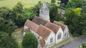 An aerial view of a church with a bell tower, surrounded by trees and a cemetery.