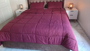 Een net opgemaakt bed met een gebonden hoofdbord, twee nachtkastjes met lampen en een marmeren vloer.