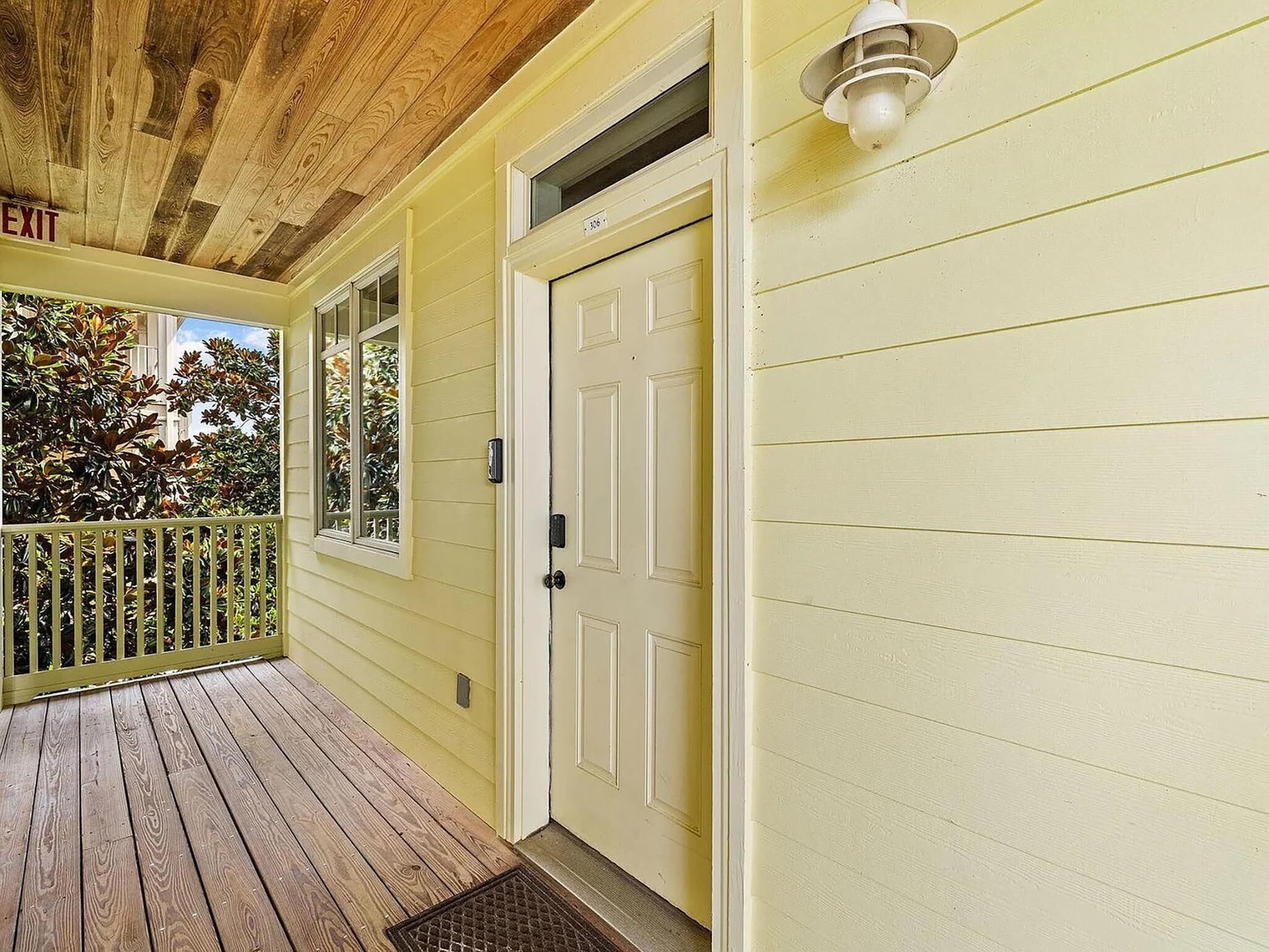 A yellow house with a wooden porch, a white door, and a small window.
