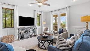 A spacious living room with a ceiling fan, a flat-screen TV, and a comfortable seating area with sofas and a coffee table. - Grand Isle Condo 306 (Santa Rosa Beach)