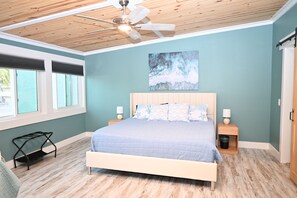 A bedroom with a bed, wooden floor, ceiling fan, windows, and artwork. - 3BR Coastal Retreat – 1 minute walk to beach - Free parking for 3 (Panama City)