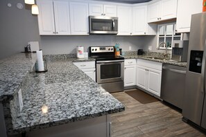 A modern kitchen with white cabinets, granite countertops, stainless steel appliances, and a wood floor. - 3BR Coastal Retreat – 1 minute walk to beach - Free parking for 3 (Panama City)
