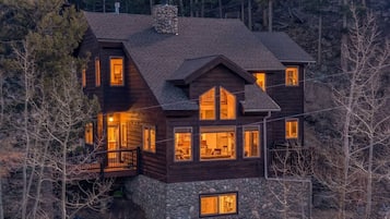 Une cabane en rondins à plusieurs étages, dotée de nombreuses fenêtres, de fondations en pierre et d’un balcon.