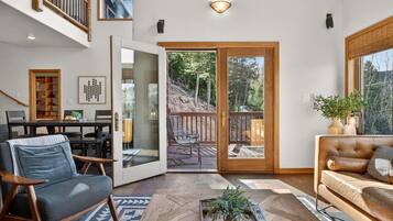 Un vaste espace de vie comprenant un grand salon avec une table basse en bois, un canapé en cuir et un coin repas donnant sur une terrasse grâce à une porte vitrée.