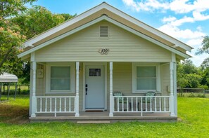 A single-story house with a gabled roof, a front porch with white railings, and a number '100' displayed above the door. - Charming Updated 2 BR Cottage Peaceful Country Getaway (Forestburg)