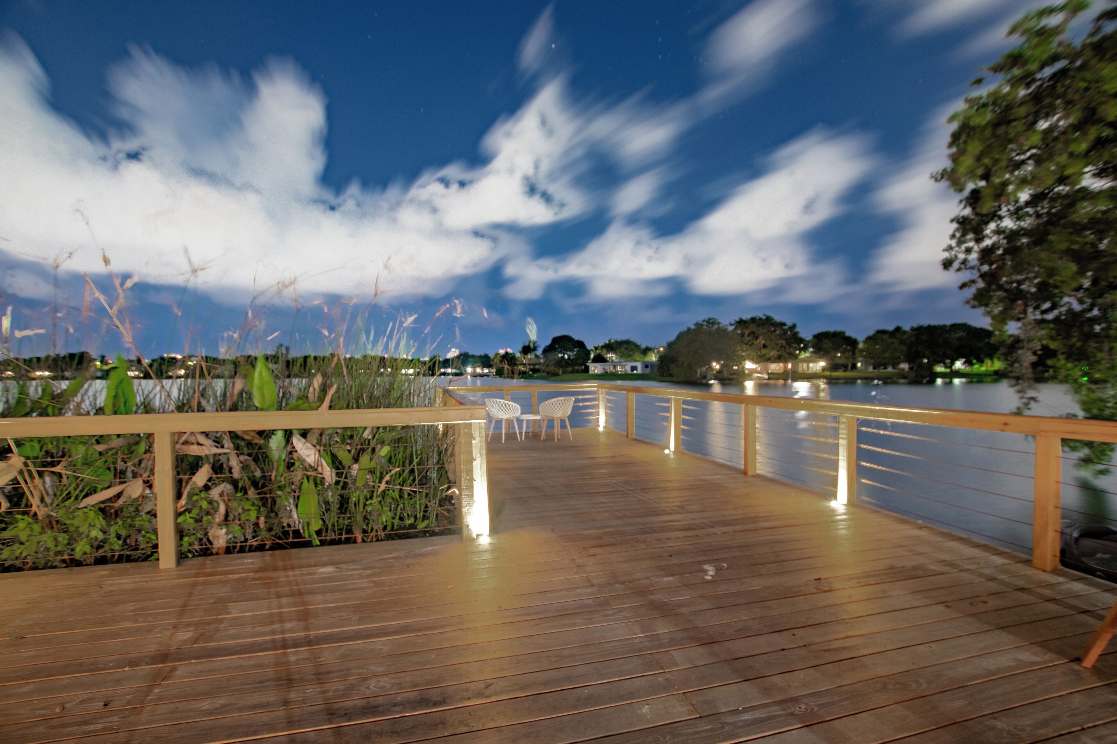 Una terraza de madera con sillas, barandilla y vista al agua y árboles.