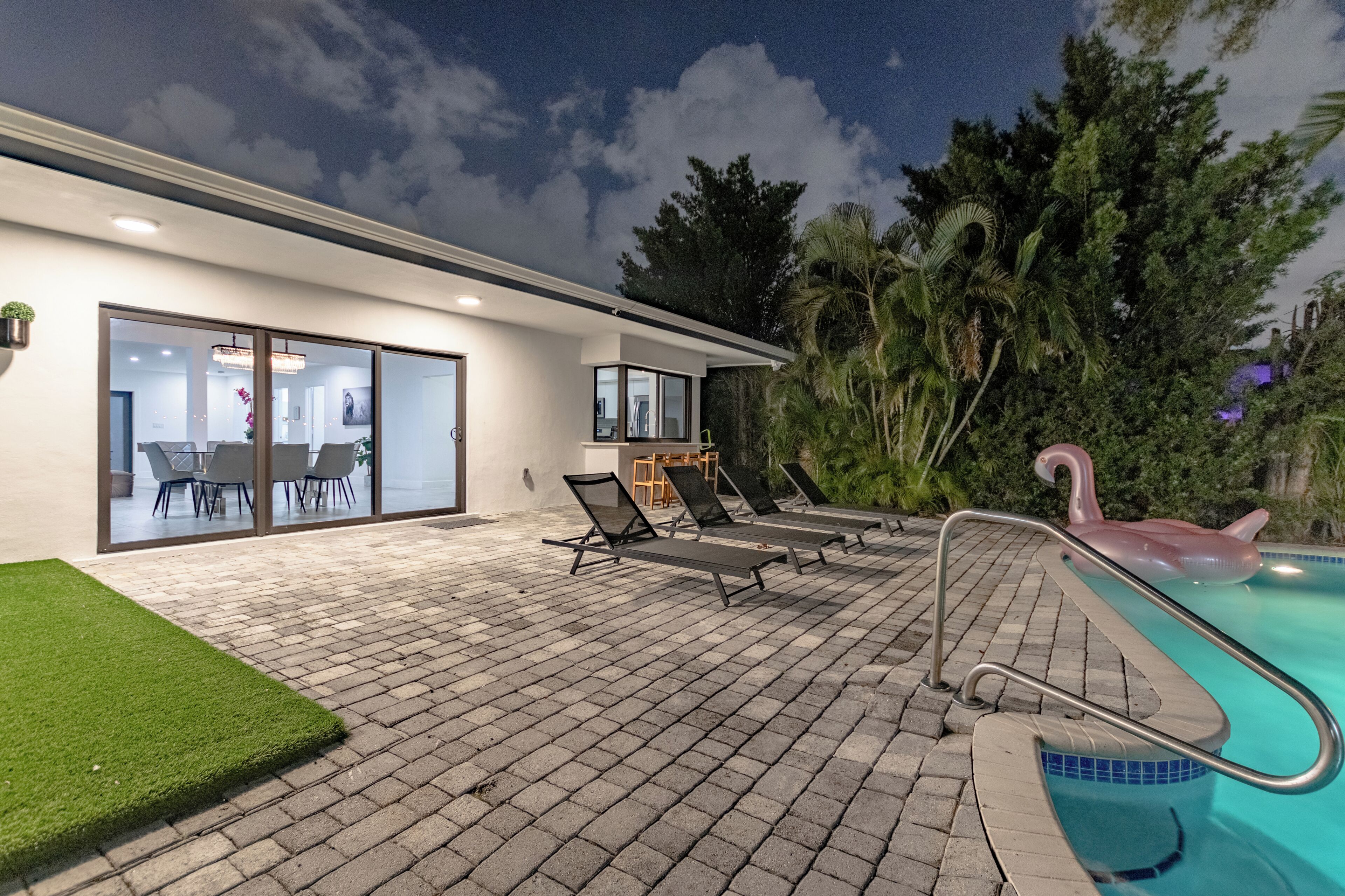 Ein modernes Haus mit Swimmingpool, Sitzgelegenheiten im Freien und einer Glastür zu einem Innenbereich.