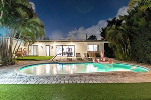 Una casa moderna con piscina, mobili da esterno e un gonfiabile a forma di fenicottero.