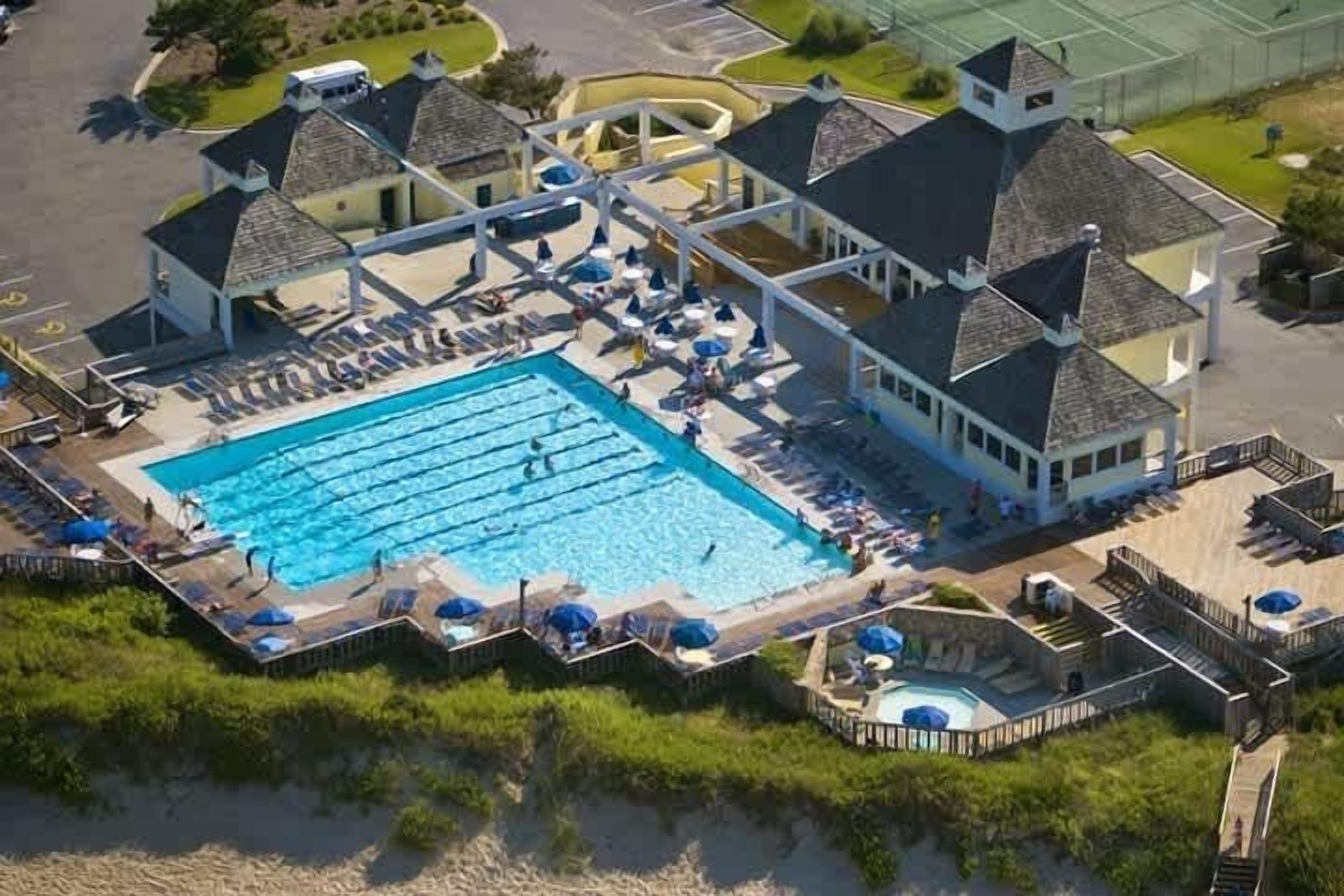 An aerial view of a resort with a large swimming pool, multiple lounge areas, and a covered deck.