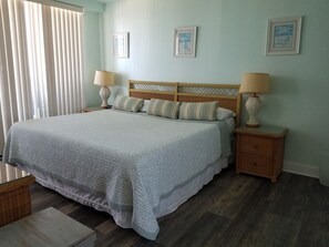 A neatly arranged bedroom with a large bed, two bedside tables with lamps, and a window with blinds. - Oceanfront 2BR • North End Boardwalk • Private Balcony • Pool • New to VRBO (Virginia Beach)