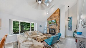 A modern living room with a stone fireplace, a large window, and a dining area. - Sundance - Lakefront w/ Private Dock (Moneta)