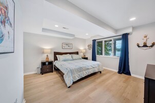 A bedroom with a bed, nightstands, a window with curtains, and a wall-mounted anchor decoration.
