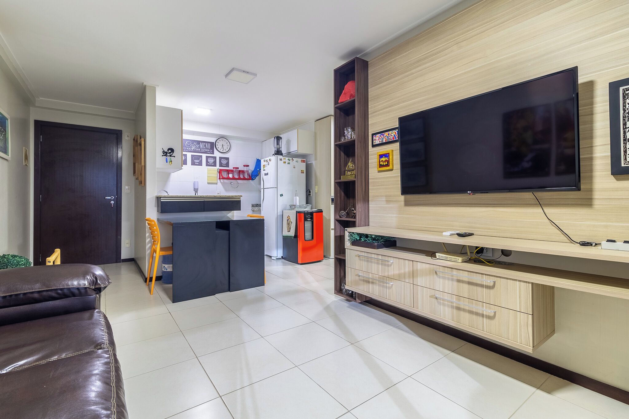 Una sala de estar moderna con televisor, sofá, área de cocina con refrigerador y mesa de comedor.