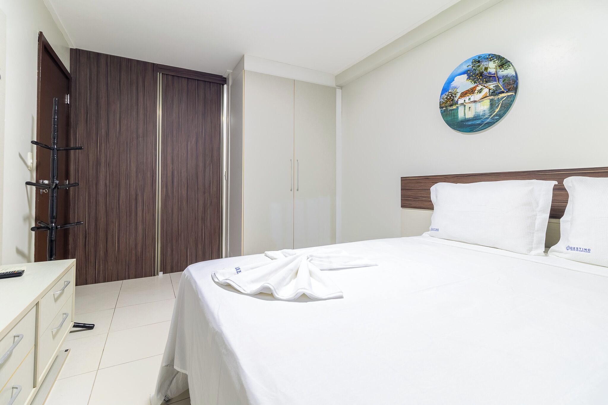 A hotel room with a bed, a wardrobe, a desk, and a painting on the wall.