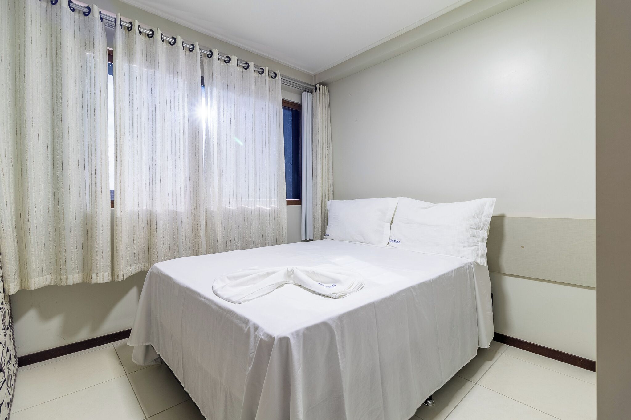 Una cama bien hecha en una habitación de hotel, con una pared lisa y una ventana con cortinas.