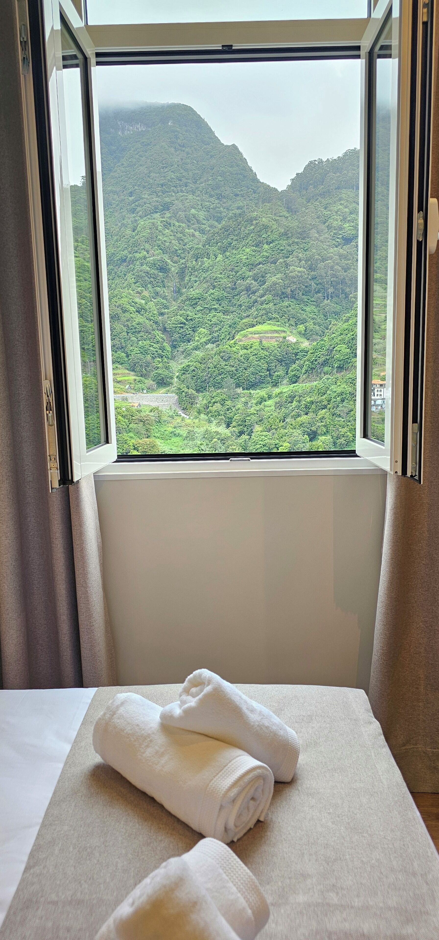 Een hotelkamer met een bed, een raam met uitzicht op een groen landschap en een paar handdoeken op het bed.